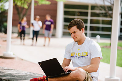 Photo of a student working on his laptop while sitting outside. Link to Closely Held Business Stock.